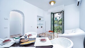 A modern, white-themed room with a dining area, a sofa, and a view of a balcony. - Francesca Flat   Amalfi (SA)