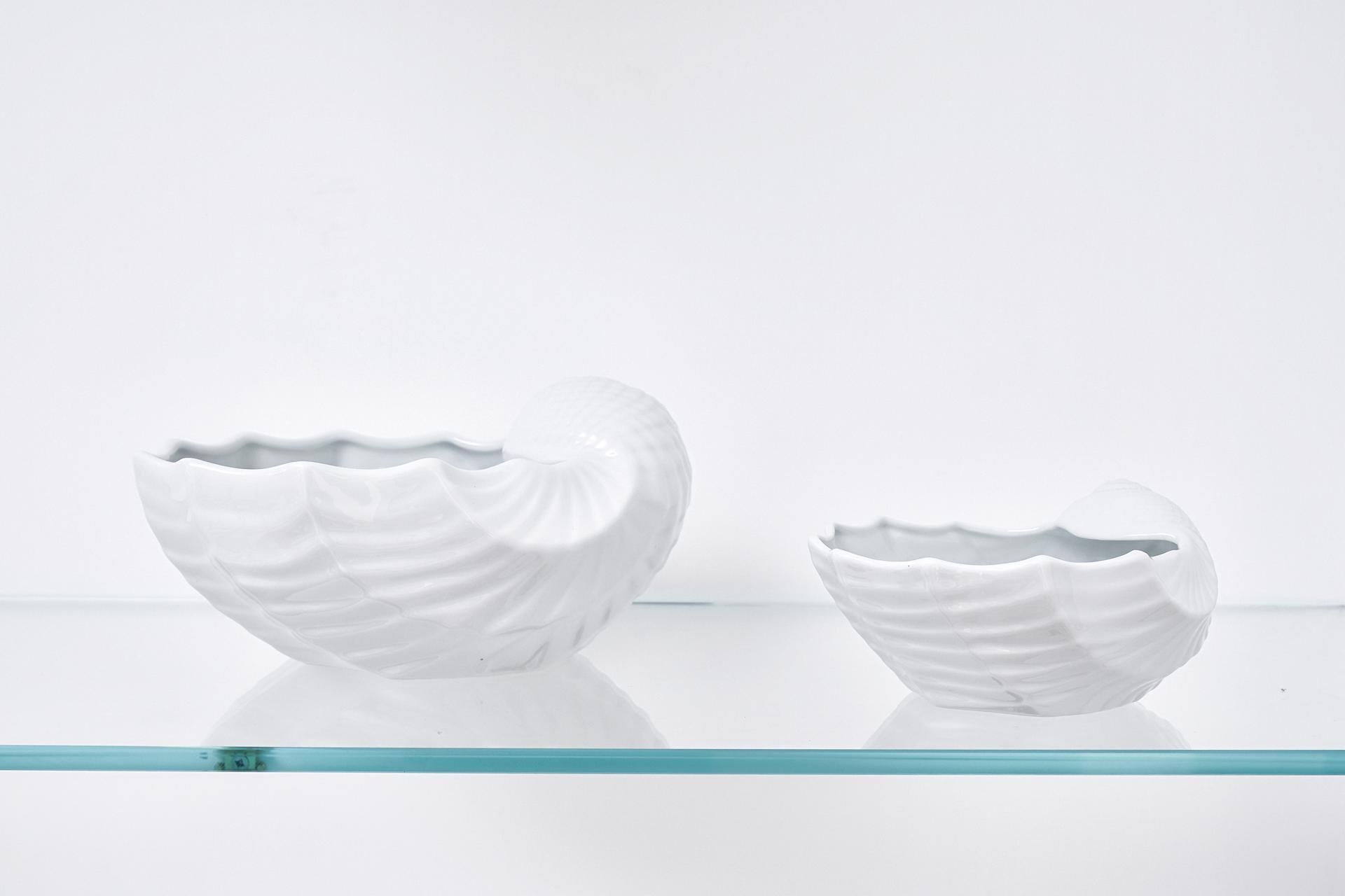 Deux bols en céramique blanche, posés sur une étagère en verre, sur un fond uni.