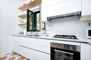 A modern kitchen with white cabinetry, a stainless steel sink, a gas stove, and an oven. - Francesca Flat   Amalfi (SA)