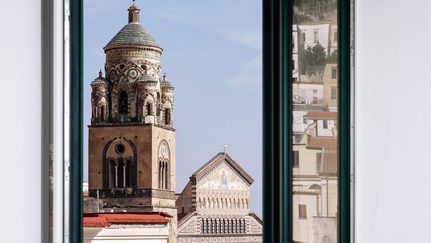 A view of a historic building with a prominent tower and a smaller adjacent structure, through a window. - Francesca Flat   Amalfi (SA)