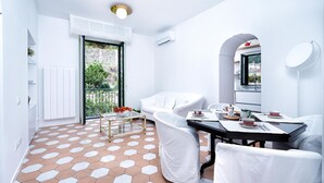 A modern dining area with a white table, chairs, and a view of greenery outside. - Francesca Flat   Amalfi (SA)