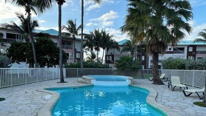 A swimming pool with a stone border, surrounded by palm trees and a white fence.