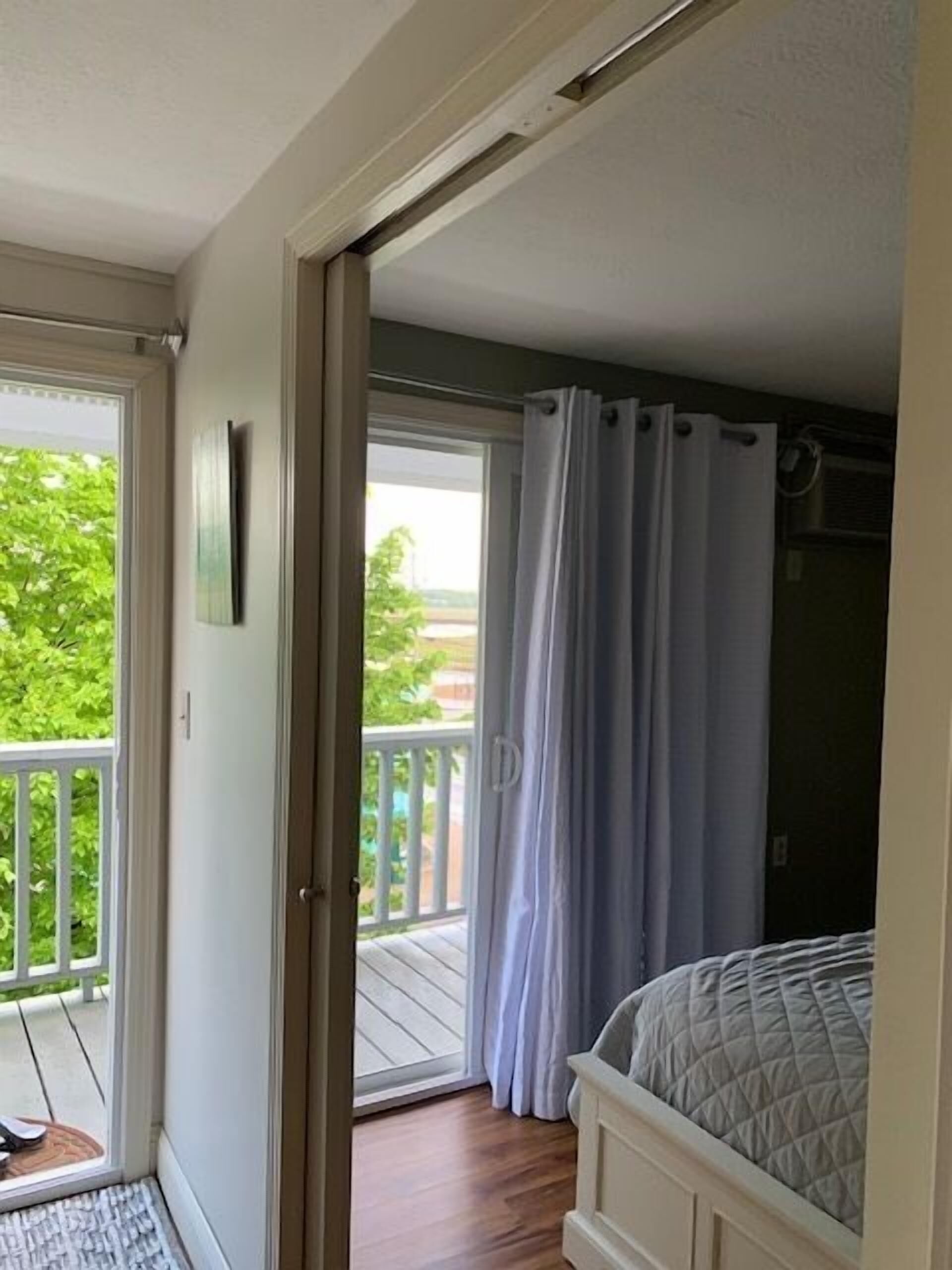 A bedroom with a bed, a sliding glass door leading to a balcony, and a view of greenery outside.