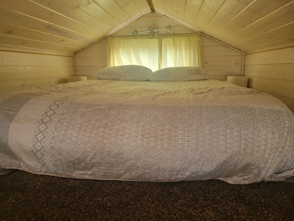 Un dormitorio con cama, ventana con cortinas y techo de madera.