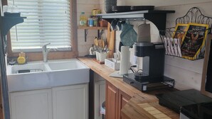 A compact kitchen with a wooden countertop, a sink, and a refrigerator. There are various kitchen utensils and appliances, including a coffee maker and a kettle. - "Tiny Home" at Buena Vista Lavender Farm with private porch and a stunning view (Silverton)