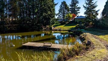 A serene lakeside setting with a wooden dock extending into the water, surrounded by lush greenery and tall trees.