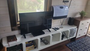 A television on a white stand with a window above it, a white cabinet with drawers, and a small plant on top. - "Tiny Home" at Buena Vista Lavender Farm with private porch and a stunning view (Silverton)