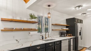A modern kitchen with a marble countertop, black cabinets, and a stainless steel refrigerator. - 6BR Designer Home in Massanutten with Hot Tub, Sauna (McGaheysville)