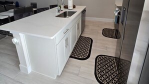 A modern kitchen with white cabinetry, a central island with a sink, a stainless steel refrigerator, and a dining area with a table and chairs. - Charming 3-bedroom townhome with WiFi, AC in Reunion Resort, Kissimmee, FL
 (Kissimmee)