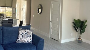 A living room with a blue sofa, a round mirror, a white door, and a potted plant. - Charming 3-bedroom townhome with WiFi, AC in Reunion Resort, Kissimmee, FL
 (Kissimmee)