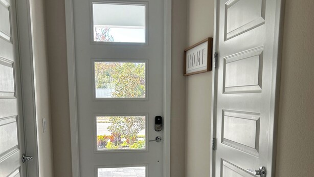 A hallway with a white door featuring a frosted glass panel, a small window, and a doorbell. The floor is tiled, and there is a 'HOME' sign on the wall. - Charming 3-bedroom townhome with WiFi, AC in Reunion Resort, Kissimmee, FL
 (Kissimmee)