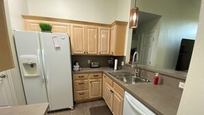 A compact kitchen with a refrigerator, a water dispenser, a sink, and wooden cabinets.