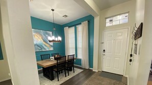 A dining area with a wooden table and chairs, a painting on the wall, and a ceiling light fixture.