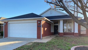 A two-story house with a white garage door, a brick exterior, and a front porch.
