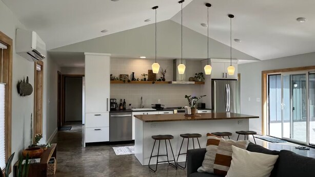 A modern kitchen with a central island, bar stools, and pendant lighting. - The North Oak, a Modern Cabin (Washburn)
