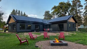 A modern house with a fire pit and red chairs in the yard. - The North Oak, a Modern Cabin (Washburn)