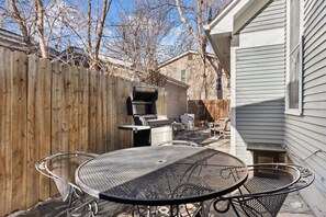 Un jardin avec une table et des chaises en métal, un barbecue et une clôture en bois.