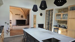 Une cuisine moderne dotée d’un îlot central, de luminaires suspendus noirs et d’un pare-feu en pierre.