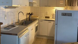 Een kleine keuken met witte kasten, een spoelbak, een fornuis en een koelkast.