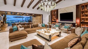 A spacious living room with a large TV, comfortable sofas, and a chandelier. - Quivira/Cabo Golf Course Villa W/Awesome OceanView, Infinity Pool on Fairway 18  (Cabo San Lucas)