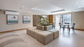 A modern hotel lobby with a sectional sofa, a dining area with chairs and a table, and two framed pictures on the wall.