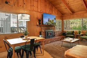 A cozy interior with a fireplace, wooden walls, a dining area, and large windows.