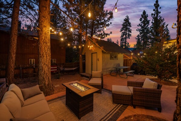 A cozy outdoor seating area with a fire pit, wicker furniture, and string lights.