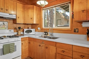Une cuisine avec des meubles de rangement en bois, un four à micro-ondes, un évier et une cuisinière.