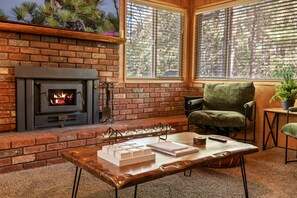 A cozy living room with a fireplace, a green armchair, and a coffee table with books and candles.