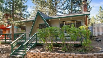 Een chalet met een groen dak, een bakstenen fundering en een houten terras.