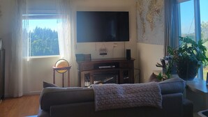Una sala de estar con un televisor de pantalla plana grande, un sofá, una mesita y una planta en maceta.