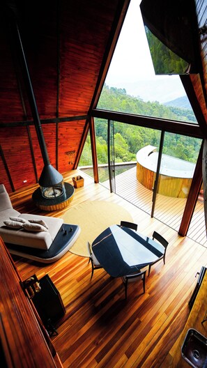 Interior acollidor d'una cabana amb terra de fusta, una taula de dinar i un sofà. Un finestral gran ofereix vistes a un paisatge forestal.