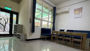 A spacious room with a large window, a blue bench, a wooden table, and an air conditioning unit on the wall. - Yilan Hall 2 (Jincheng)