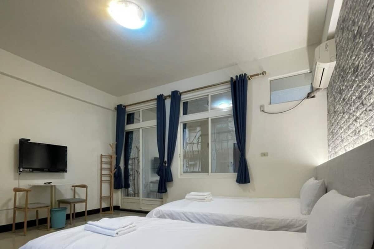 Una habitación de hotel con dos camas, un televisor y un ventanal con cortinas.