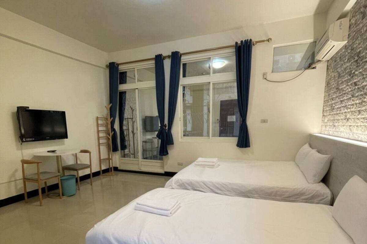Habitación de hotel con dos camas, televisión, ventana con cortinas, una escalera y un cubo de basura.