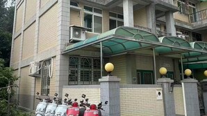 A multi-story building with a green roof, air conditioning units, and a row of parked scooters. - Yilan Hall 2 (Jincheng)