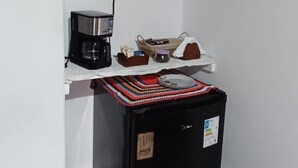 Ett kompakt kök med kylskåp, mikrovågsugn, kaffebryggare och en liten papperskorg.