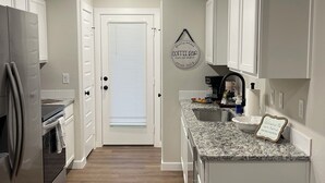 A modern kitchen with white cabinets, a granite countertop, and a stainless steel refrigerator.