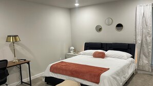 A neatly arranged bedroom with a bed, bedside tables, a desk, and a chair.