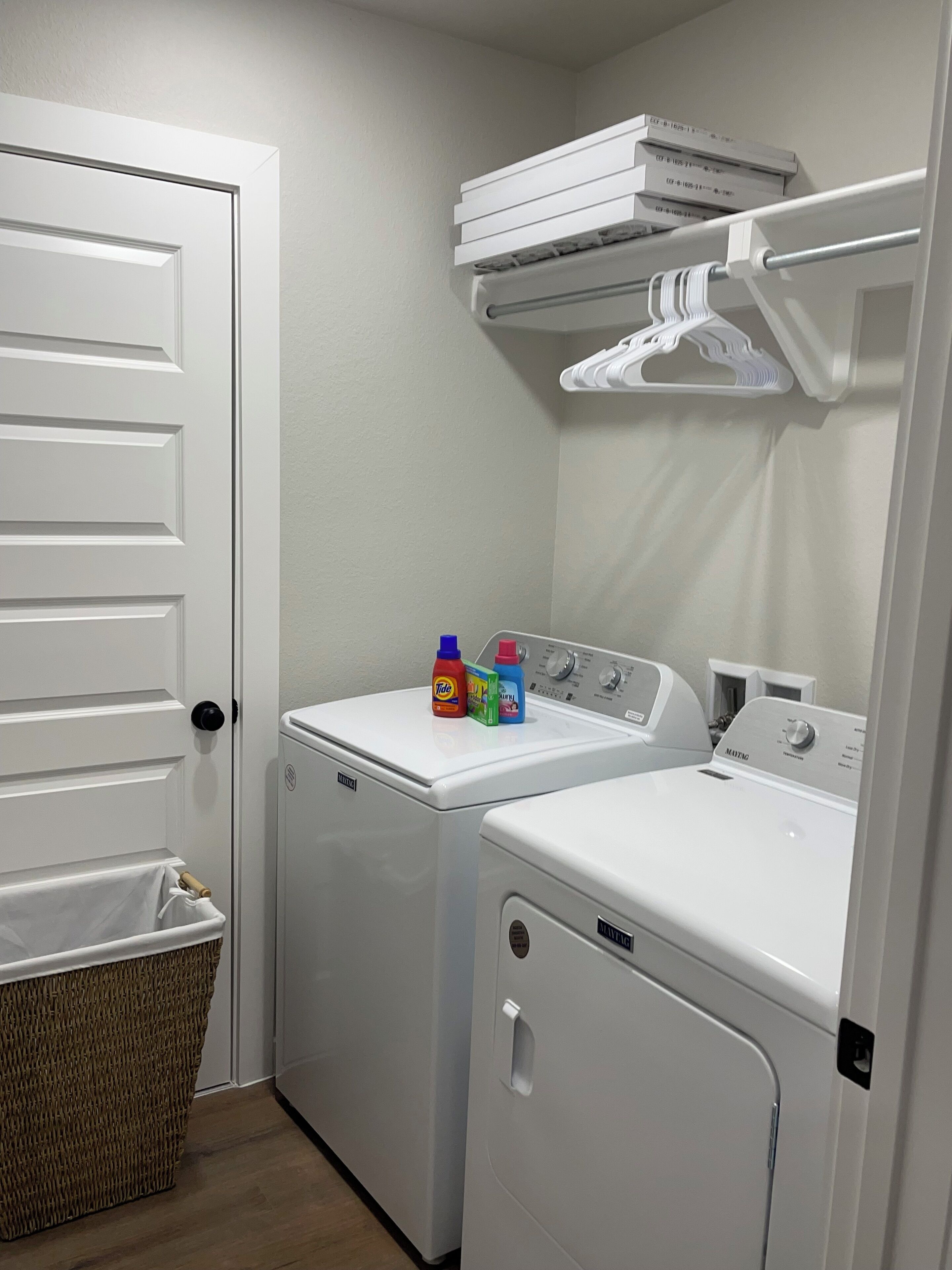A laundry room with two white front-loading washing machines, a drying rack, and a basket.