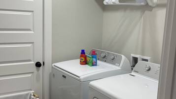 A laundry room with two white front-loading washing machines, a drying rack, and a basket.