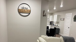 A modern living room with a white leather sofa, a grey throw blanket, and a kitchen in the background.