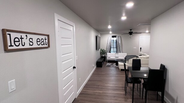 A modern living room with a dining area, a white door, and a sign that reads "let's eat".