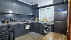Una cocina moderna con armarios oscuros, lavadora integrada y refrigerador.