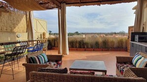 Un patio exterior con mobiliario de mimbre, una mesa y una cocina con pileta y electrodomésticos.