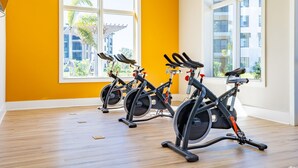 A gym with three stationary bikes, large windows, and a wooden floor. - Landing Palmetto Apartments (Palmetto)