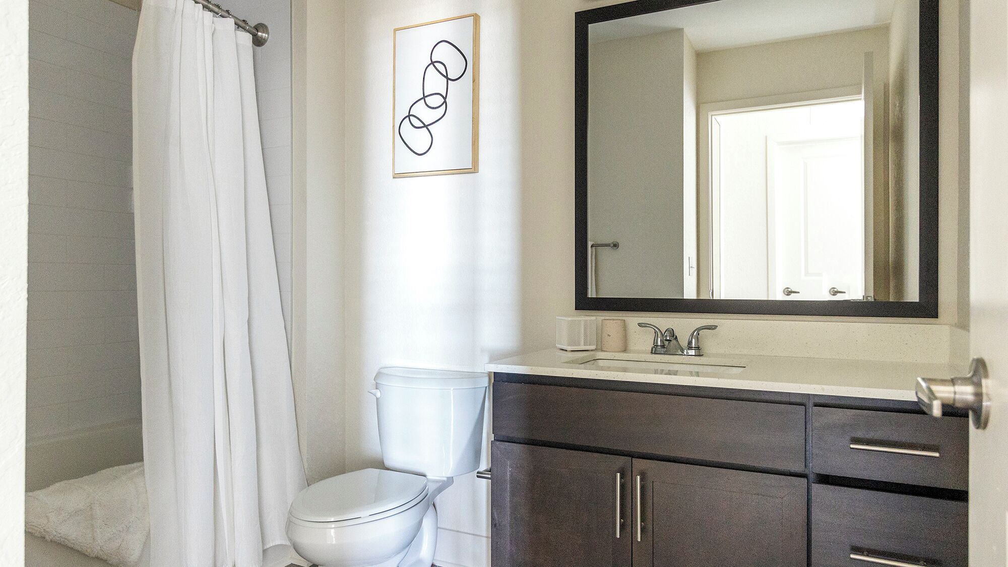 A bathroom with a white toilet, a dark wooden cabinet, a white sink with a mirror above it, and a shower curtain.