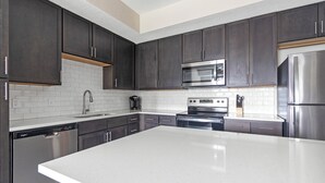 A modern kitchen with dark cabinets, a stainless steel refrigerator, a microwave, an oven, and a dishwasher. - Landing Palmetto Apartments (Palmetto)