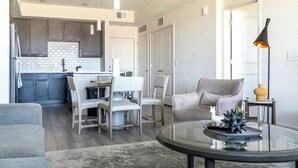A modern living room with a glass coffee table, grey sofa, and a dining area with a white table and chairs. - Landing Palmetto Apartments (Palmetto)