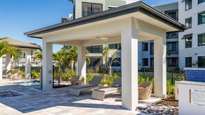 A covered outdoor seating area with lounge chairs and a pool. - Landing Palmetto Apartments (Palmetto)